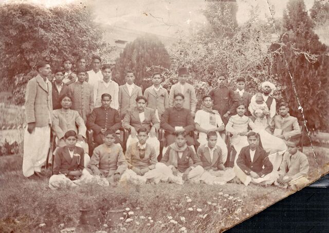 A class of young men outdoors in three rows, some seated on chairs.