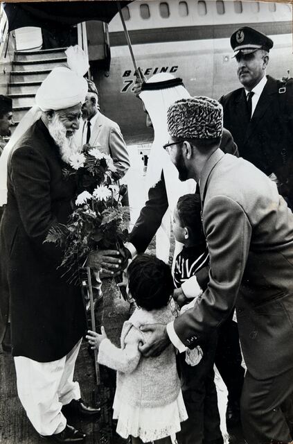 Hazrat Khalifatul Masih III at the foot of the aircraft steps, receiving flowers from two children.