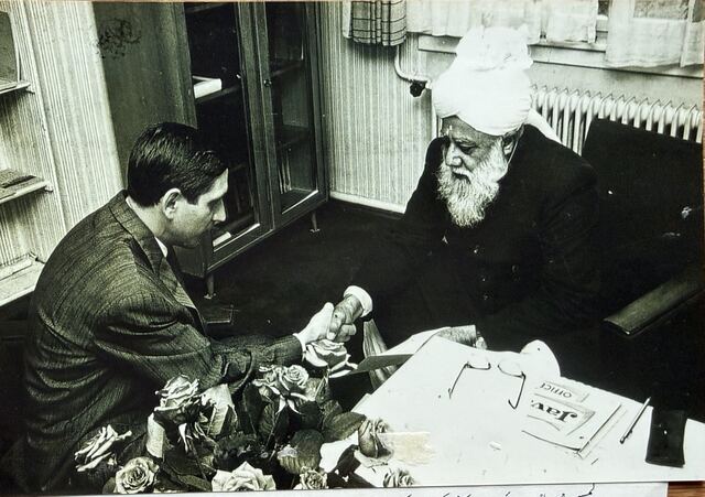 A young man taking the pledge at a table with Hazrat Khalifatul Masih III.
