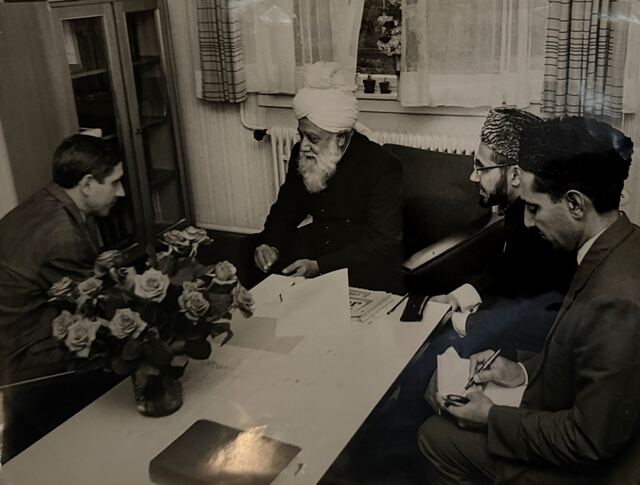 Hazrat Khalifatul Masih III at a table with a young man and two others.