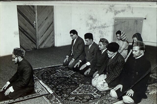 The imam and worshippers seated in prayer on carpets.