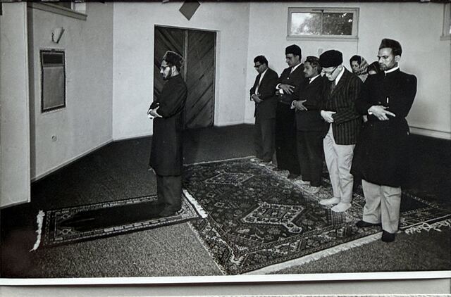 An imam standing in front of a row of worshippers.