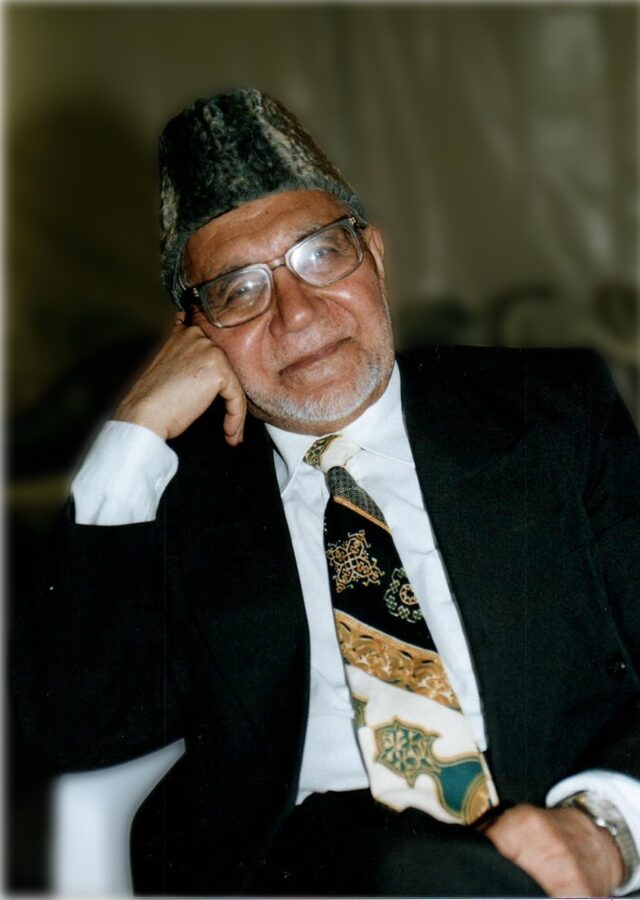 Maulana Fazal Ilahi Anweri in his later years, seated, in a karakul cap and dark suit, smiling.